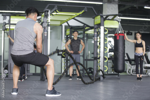 Young man exercising with battling rope at gym