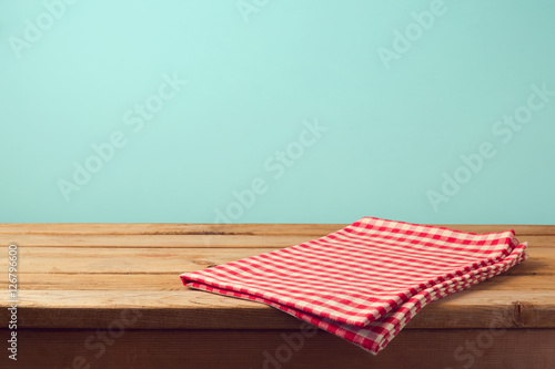 Empty wooden deck table and red checked tablecloth over mint wallpaper background