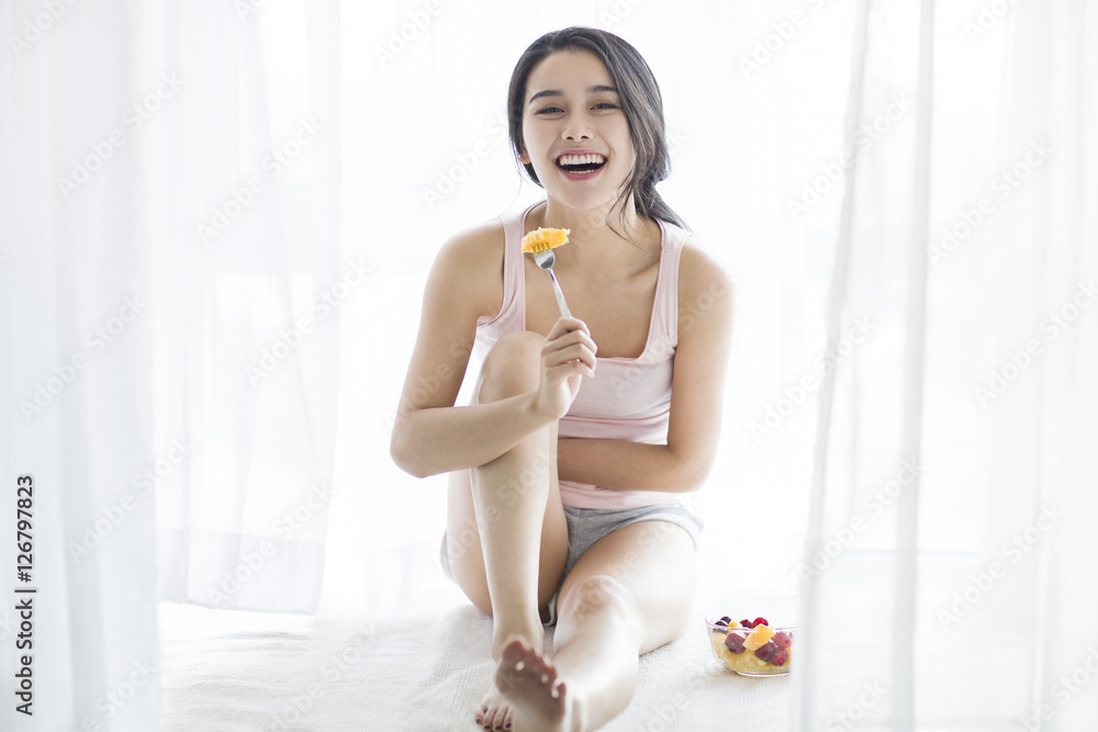 Happy young woman eating fruit salad on window sill Happy young woman eating fruit salad on window sill