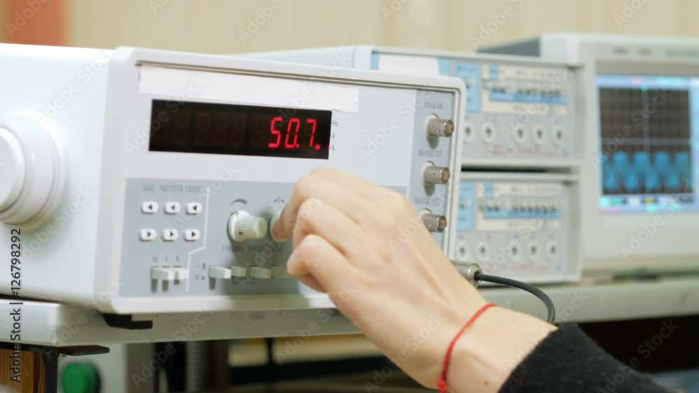 Woman engineer student adjusts the electric generator by hand. It changes the numbers on the device and carefully watching for indications. Woman engineer student adjusts the electric generator by hand. It changes the numbers on the device and carefully watching for indications.