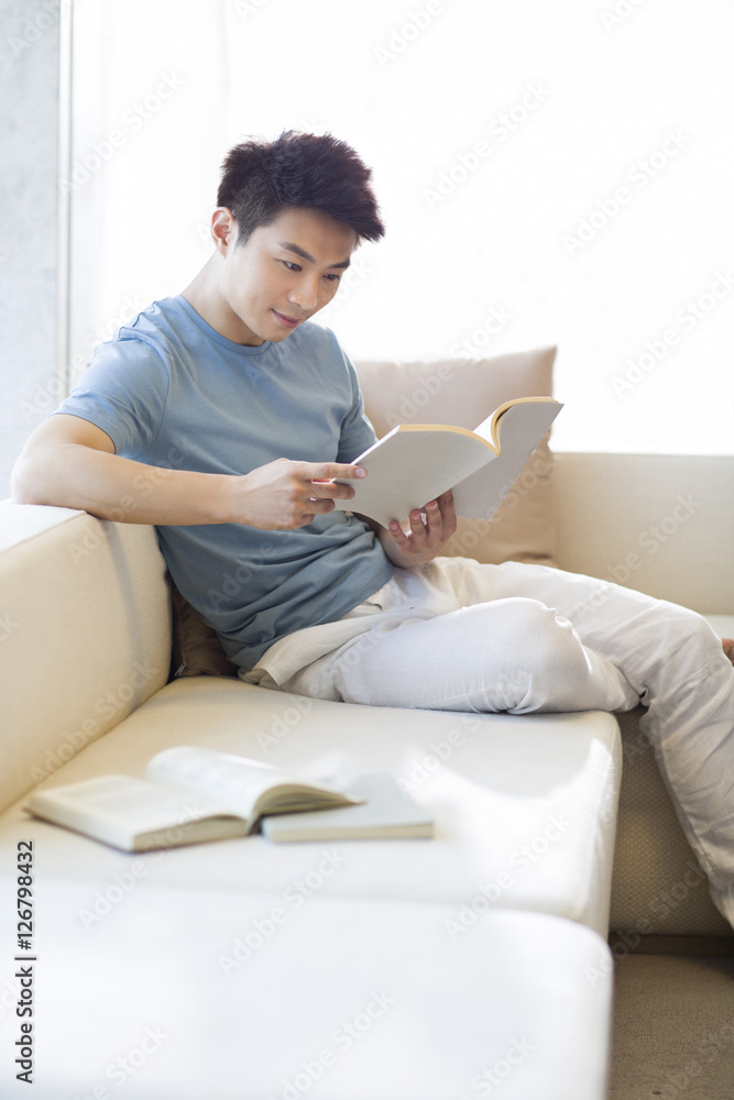 Fototapeta premium Young man reading a book on the sofa