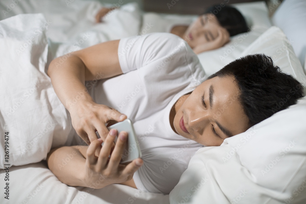 Fototapeta premium Young husband using smart phone on bed