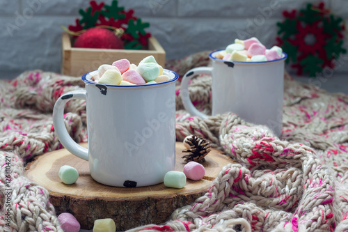 Homemade hot chocolate topped with marshmallow in enamel mug, warm scarf on background, horizontal