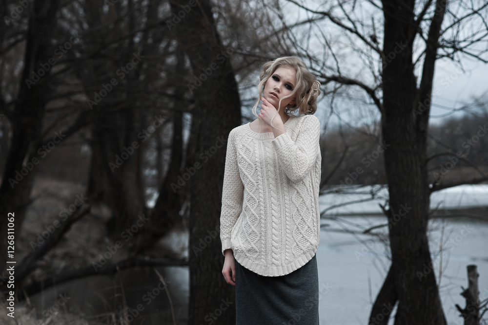 beautiful young blonde woman with blue eyes in white pullover long skirt on spring background, forest, lake, trees. Cold mood. Fashion, emotional portrait..Winter, spring, outdoor portrait. beautiful young blonde woman with blue eyes in white pullover long skirt on spring background, forest, lake, trees. Cold mood. Fashion, emotional portrait..Winter, spring, outdoor portrait.