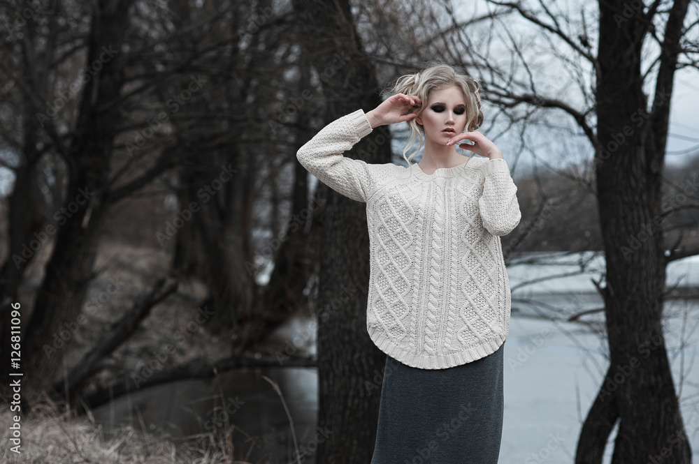 beautiful young blonde woman with blue eyes in white pullover long skirt on spring background, forest, lake, trees. Cold mood. Fashion, emotional portrait..Winter, spring, outdoor portrait. beautiful young blonde woman with blue eyes in white pullover long skirt on spring background, forest, lake, trees. Cold mood. Fashion, emotional portrait..Winter, spring, outdoor portrait.