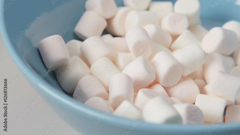 SLOW MOTION: Marshmallows fall on blue dish (close up) SLOW MOTION: Marshmallows fall on blue dish (close up)