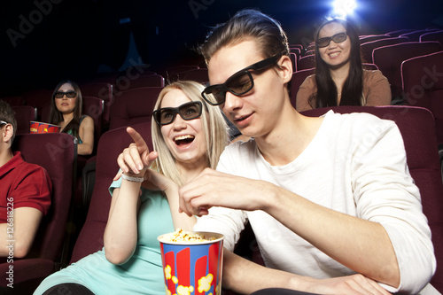 Young people sitting at the cinema, watching a film and eating p