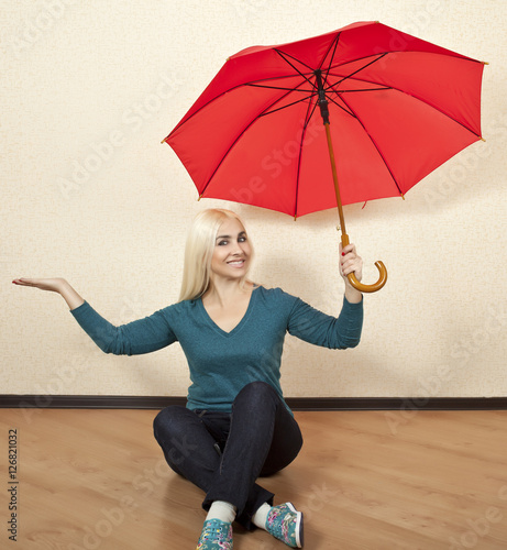 Happy blonde woman with red umbrella sitting on the floor