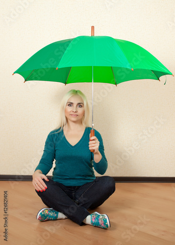 Girl with a green umbrella sits on the floor in the room
