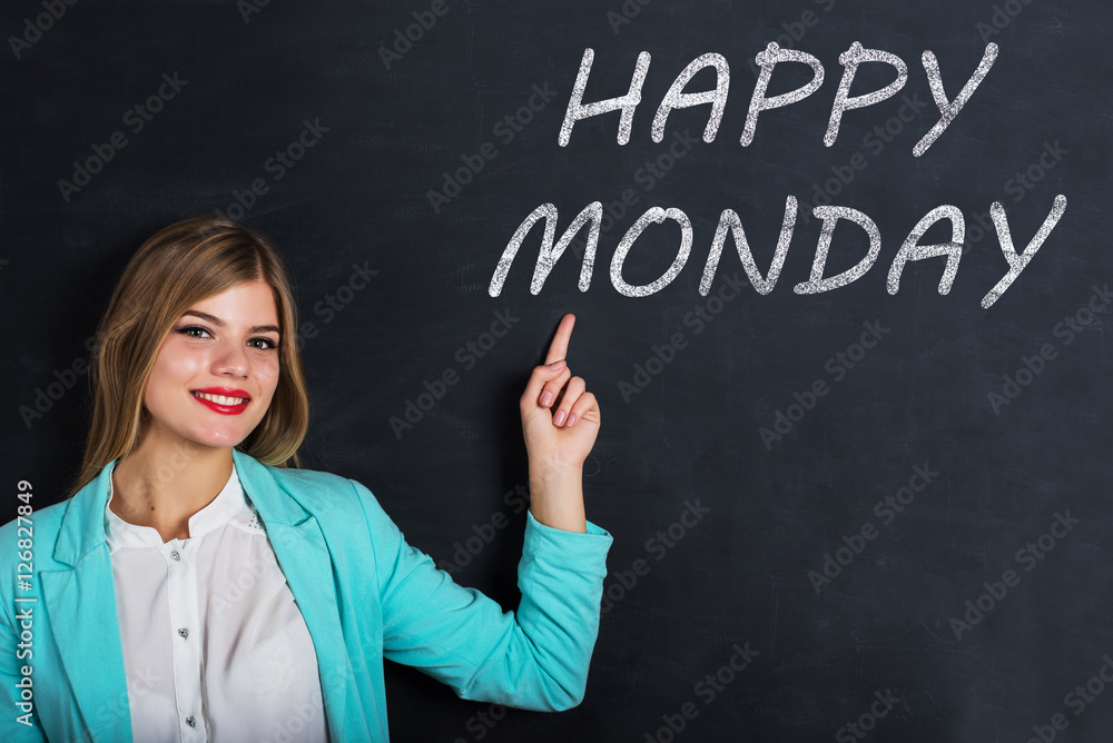 Beautiful young female student is pointing, looking at camera and smiling, standing against blackboard with text Beautiful young female student is pointing, looking at camera and smiling, standing against blackboard with text