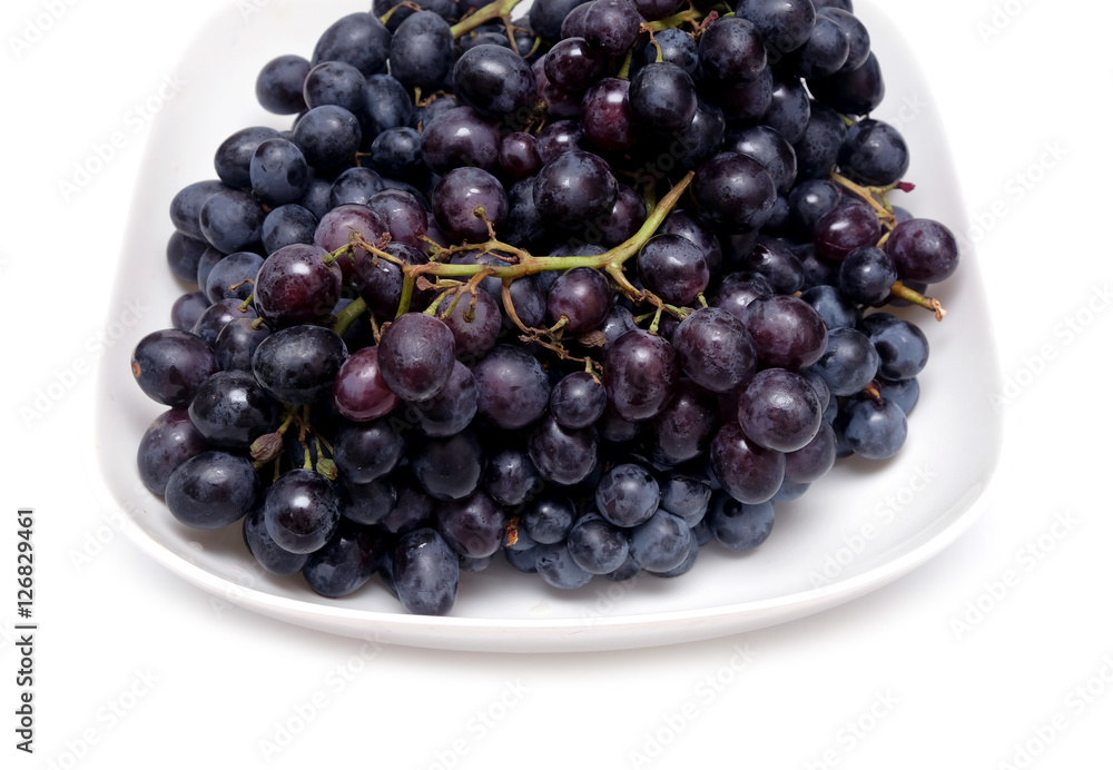 Lot of ripe black wine grape bunches with black berries in square bowl isolated on white background front view close up Lot of ripe black wine grape bunches with black berries in square bowl isolated on white background front view close up