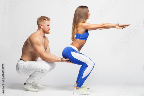 male trainer helping sexy woman doing squats isolated on white background