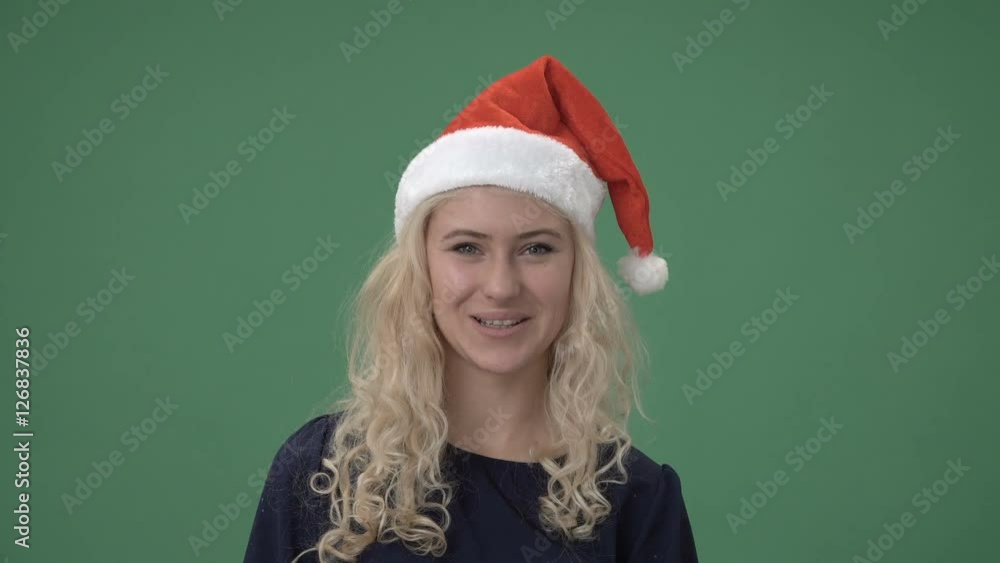 Close up young blonde woman in a santa's red cap winking and smiling, chroma key green screen Close up young blonde woman in a santa's red cap winking and smiling, chroma key green screen