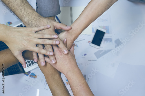 Multiethnic group of young people putting their hands on top of each other. Close up image of young students making a stack of hands with business report background