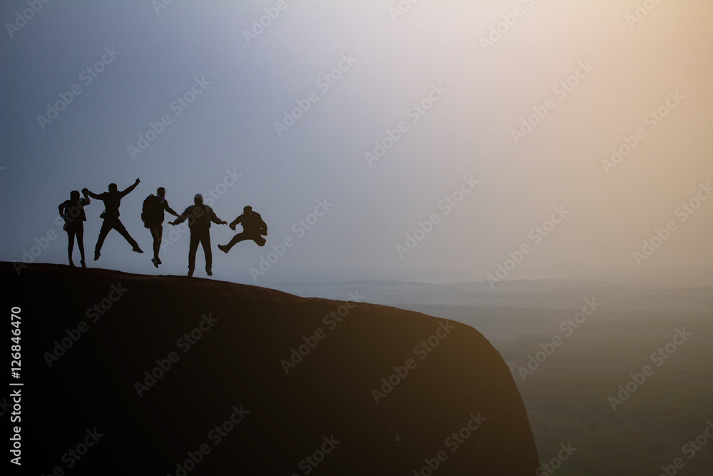 silhouette group of young jumping on the top of the mountain, sunlight