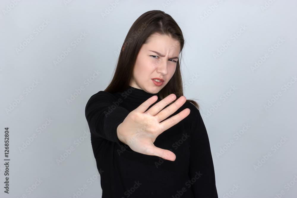 Portrait of a pretty woman in turtleneck sweater standing over gray background showing stop with one hand and looking at camera with disgust Portrait of a pretty woman in turtleneck sweater standing over gray background showing stop with one hand and looking at camera with disgust