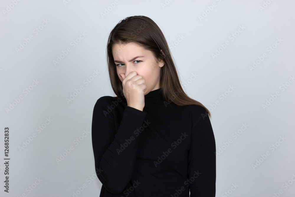 Portrait of a pretty woman in turtleneck sweater over gray background holding her nose because of a bad smell Portrait of a pretty woman in turtleneck sweater over gray background holding her nose because of a bad smell