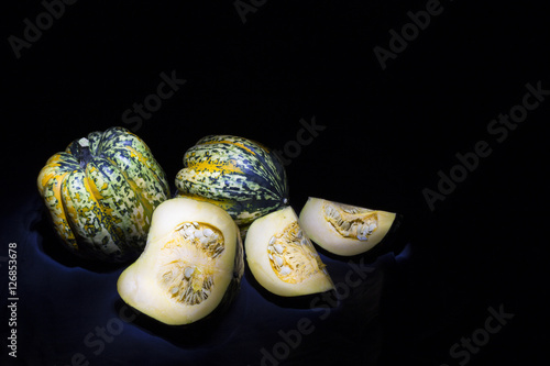 green, yellow and white speckled delicious and fresh gorgonzola pumpkins on black background. One of the pumpkins is cut into three pieces showing the seeds.