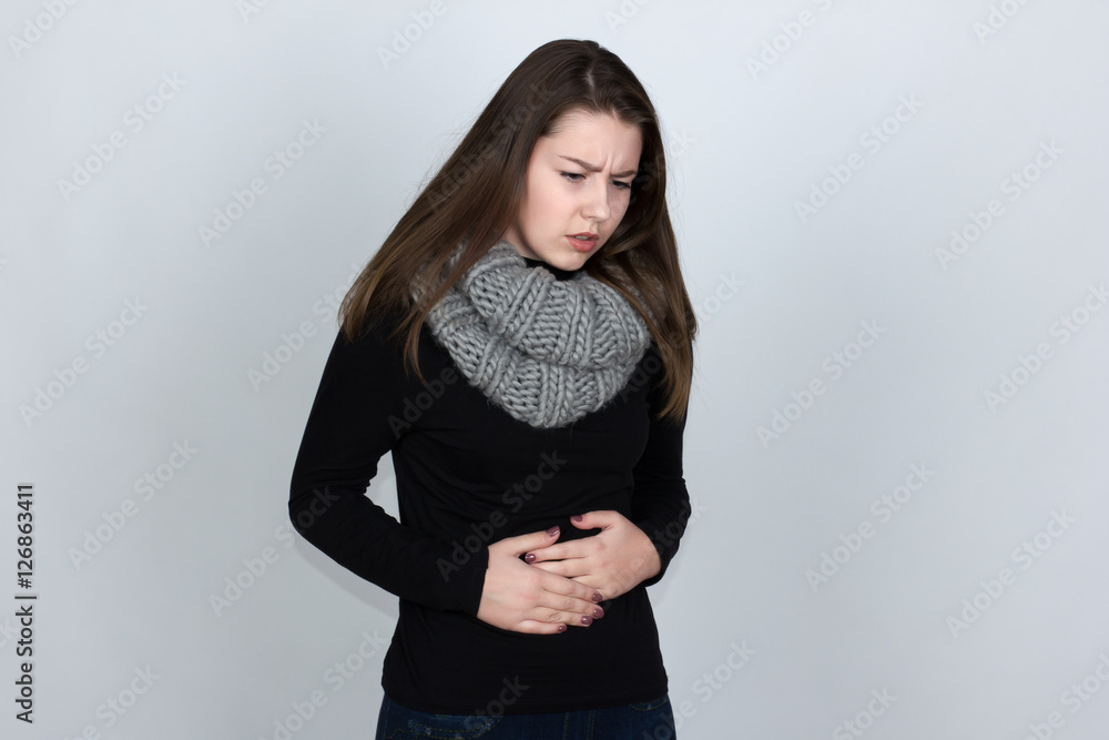 Portrait of a pretty woman in turtleneck sweater with scarf with stomach issues and standing over gray background and looking down white with red accent Portrait of a pretty woman in turtleneck sweater with scarf with stomach issues and standing over gray background and looking down white with red accent