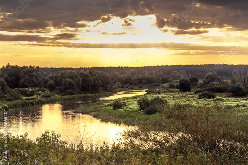 Vibrant sunrise with beautiful rural landscape at river bank with moody sky and sunlight © splendens