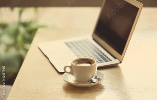 Aromatic cup of coffee and laptop on table in cafe