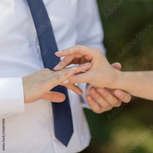 Bride putting wedding ring on finger of her groom