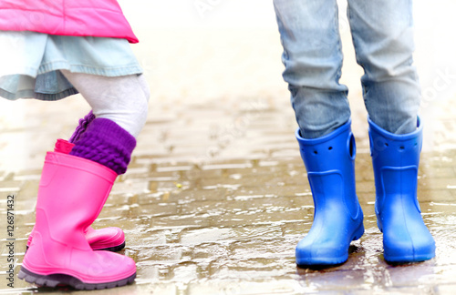 Close up view of children legs in gumboots jumping on wet pavement