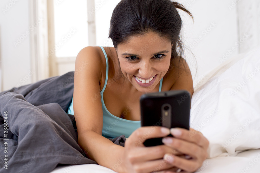 hispanic woman in bed texting internet surfing on mobile phone in social network addiction hispanic woman in bed texting internet surfing on mobile phone in social network addiction