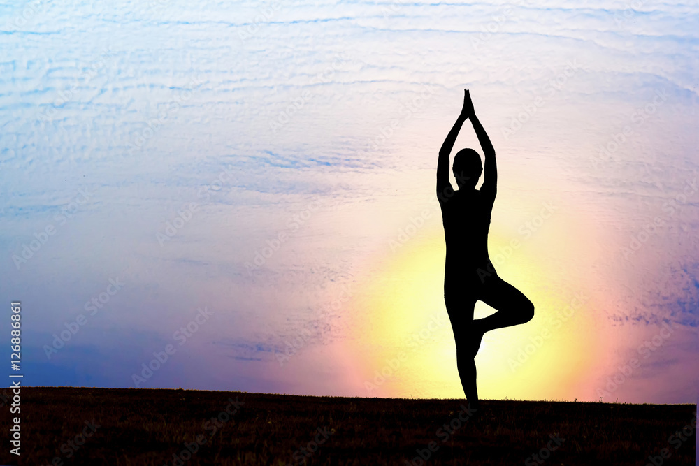 Silhouette of woman practicing yoga at sunset