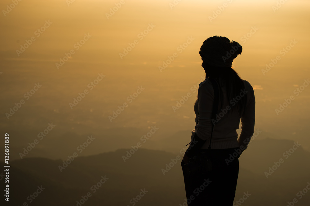 Silhouette of a  woman photographer standing in dry grass field on sunrise
