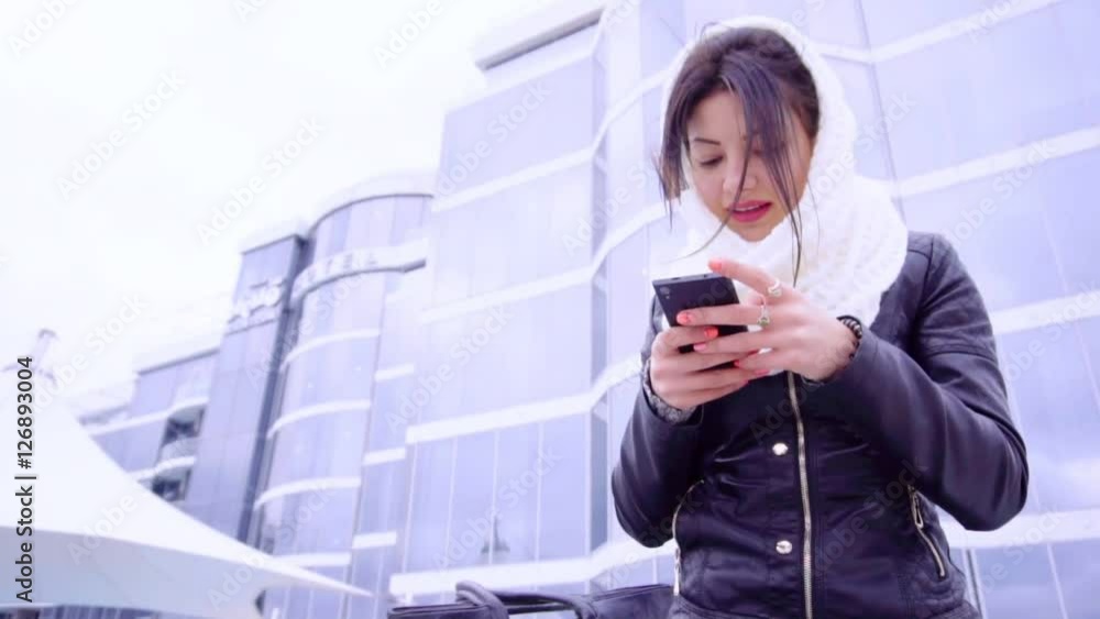Young brunette woman sits outside with her phone Young brunette woman sits outside with her phone