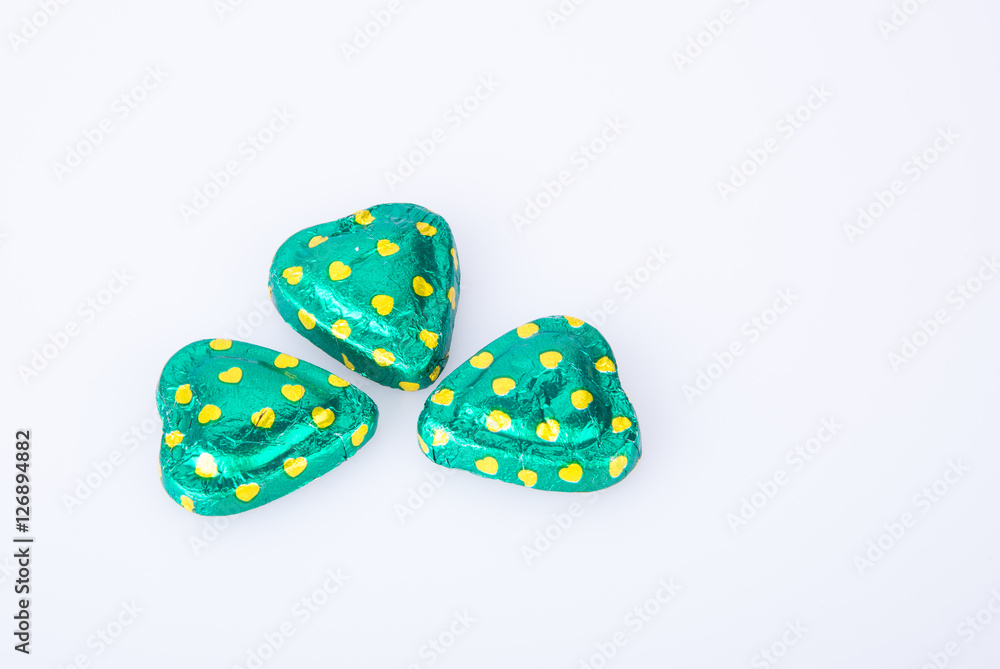 Chocolate or green foil heart-shaped chocolate on a background. Chocolate or green foil heart-shaped chocolate on a background.