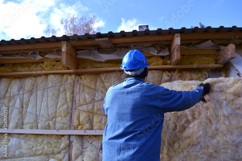 Worker with protective hat insulating wooden  house wall