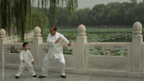 WS Grandfather and grandson doing Tai Chi in a park by lake /Beijing, China