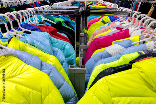 Variety of winter clothes on metal hangers. Colorful winter jackets hanging on hangers on a rack in a store