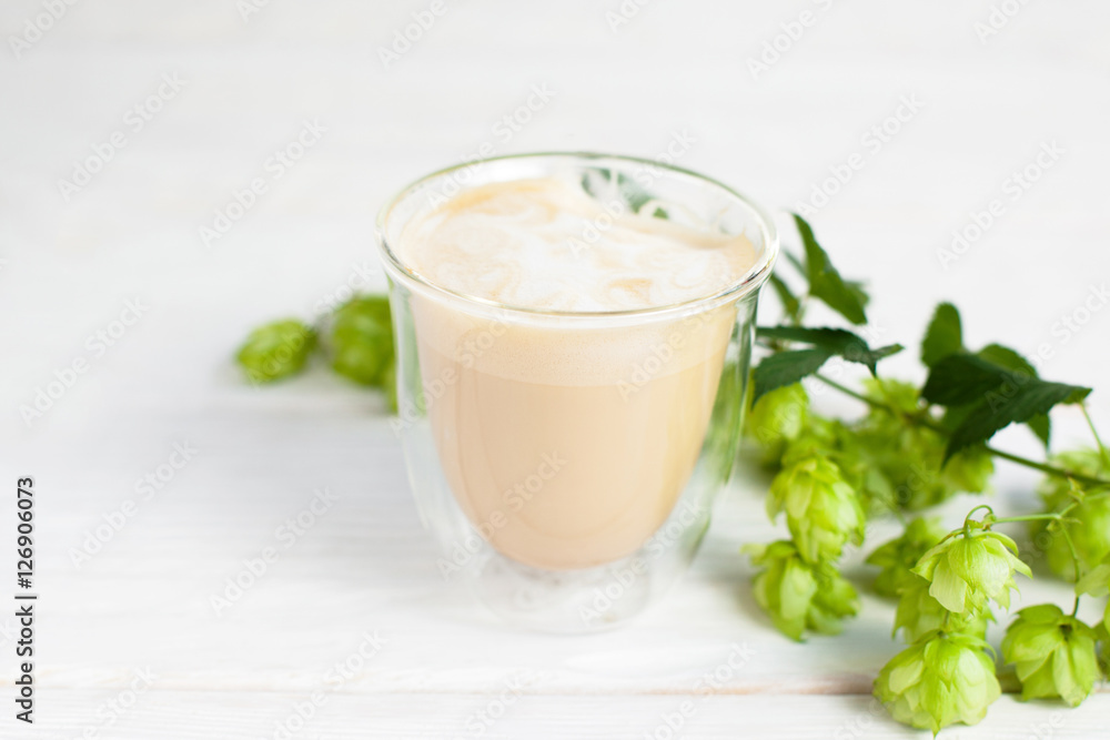Glass of latte with sprig of hop on white background. Cappuccino served in autumn style, free space for text Glass of latte with sprig of hop on white background. Cappuccino served in autumn style, free space for text