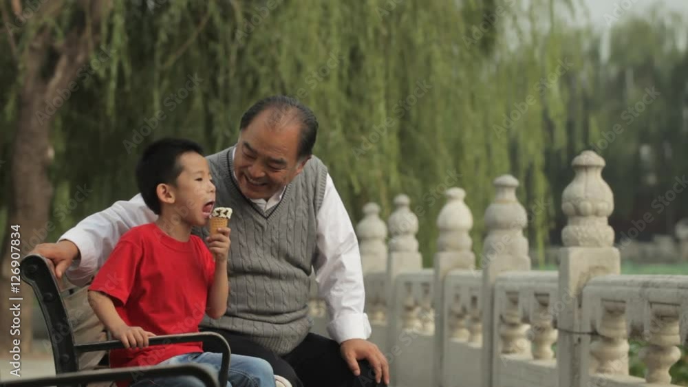 MS Young boy eating ice cream cone, sitting with his grandfather on park bench / China MS Young boy eating ice cream cone, sitting with his grandfather on park bench / China