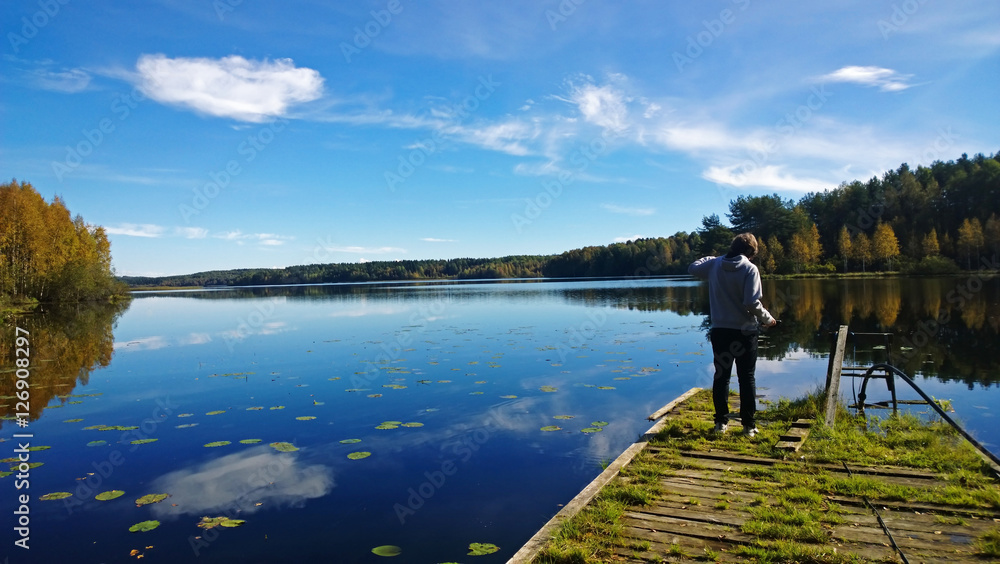 The boy takes a picture of a beautiful lake in autumn Sunny day. The view from the back