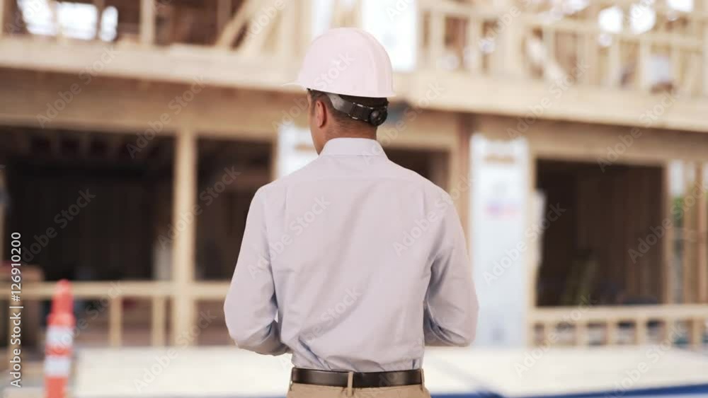 Rear view of Latino architect on construction site wearing hard hat helmet. Hispanic job foreman using tablet computer Rear view of Latino architect on construction site wearing hard hat helmet. Hispanic job foreman using tablet computer