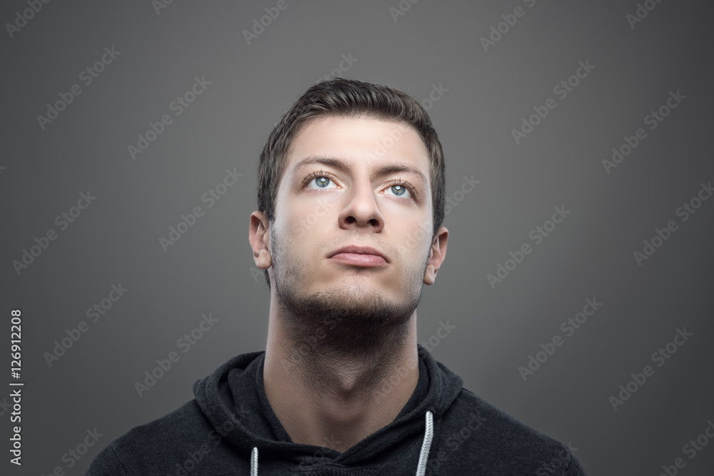 Fototapeta premium Moody portrait of young casual man looking up with illuminated face over gray background