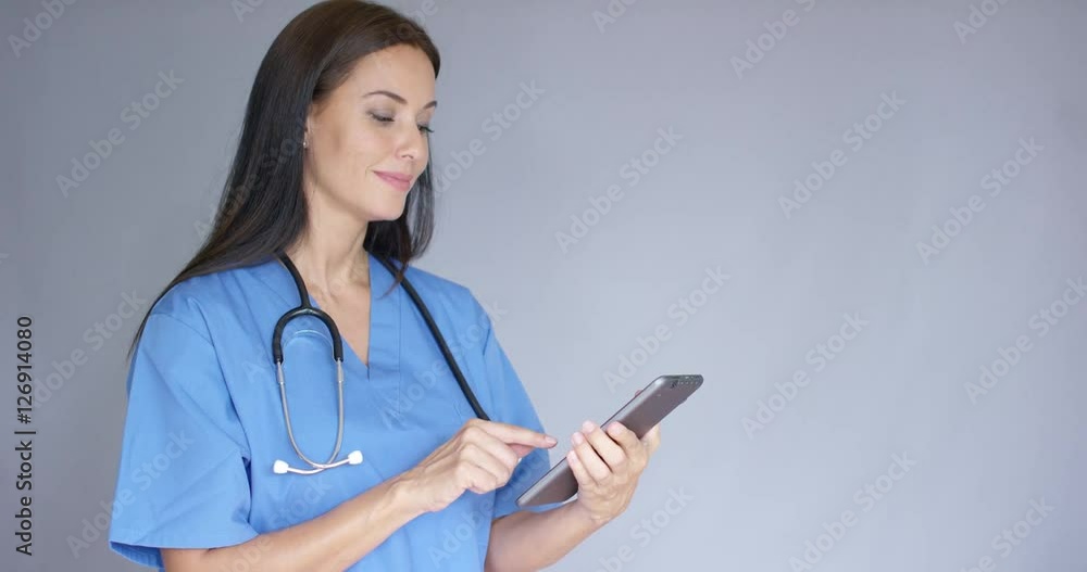 Thoughtful young woman doctor in surgical scrubs standing holding a tablet as she looks into the air with a contemplative expression with copy space Thoughtful young woman doctor in surgical scrubs standing holding a tablet as she looks into the air with a contemplative expression with copy space