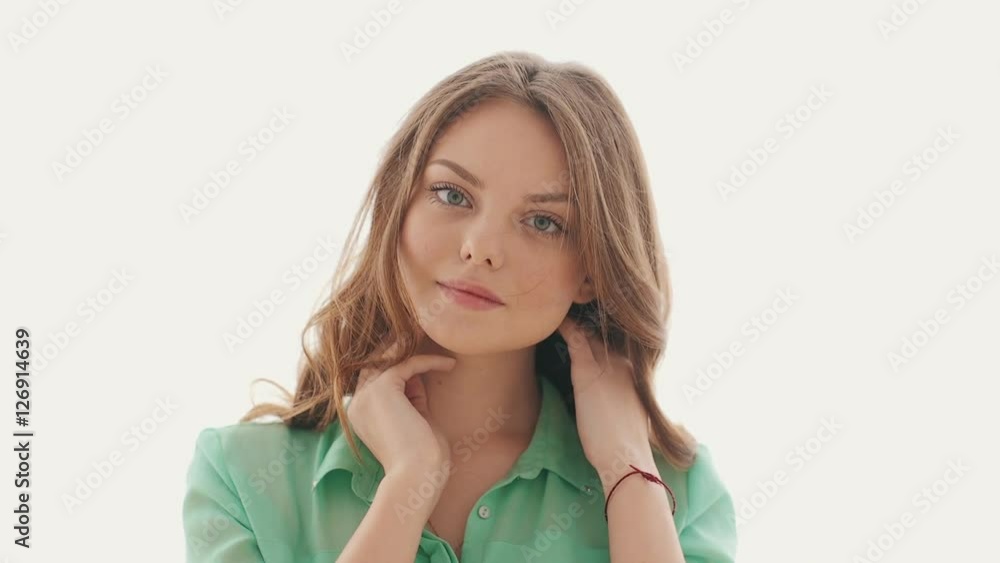 Beautiful girl looking at camera and smiling, wind flutters her hair, she touches her neck Beautiful girl looking at camera and smiling, wind flutters her hair, she touches her neck