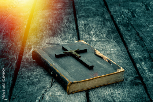 Closeup of wooden Christian cross on bible on the old table. Church utensils.