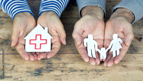 Hände halten Papierfamilie und Papierhaus mit roten Kreuz photo