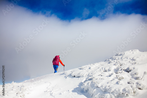Climber with backpack walks on a snowy slope.