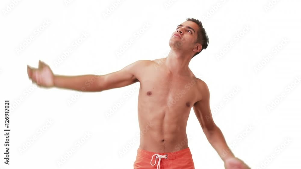 Happy Millennial Hispanic man posing in swim trunks on white background. Young guy doing silly poses having fun laughing. Happy Millennial Hispanic man posing in swim trunks on white background. Young guy doing silly poses having fun laughing.