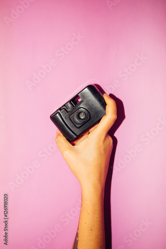 a throwaway vitage camera on hand, pink colorful background- direct flash used