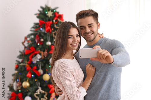 Young couple making selfie on Christmas tree background © Africa Studio