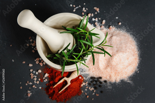 fresh rosemary in white ceramic mortar, Red Chilly powder, Himalayan salt and pepper on slate table with copy space. top view food photography