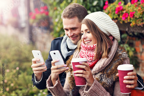 Young couple sitting on bench with coffee and smartphone